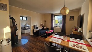 A cozy living room with a sofa, a dining table with festive tablecloths, a fireplace, and a large window with curtains. - Small apartment on the outskirts of Berlin (Teltow)