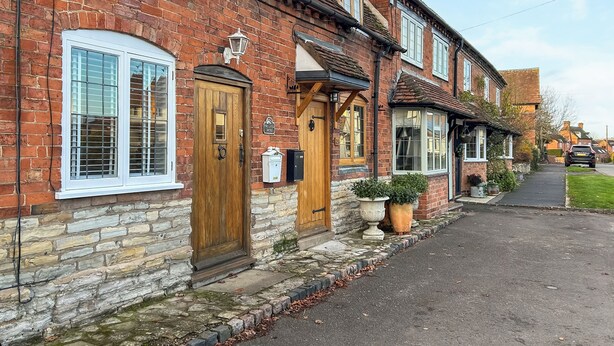 A row of traditional brick houses with stone foundations, wooden doors, and white-framed windows. - 1 bedroom accommodation in Aston Cantlow, near Stratford-upon-Avon (Aston Cantlow, near Stratford-upon-Avon)