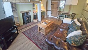 A cozy living room with a fireplace, a television, a leather sofa, and a dining area. - 1 bedroom accommodation in Aston Cantlow, near Stratford-upon-Avon (Aston Cantlow, near Stratford-upon-Avon)