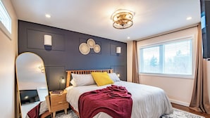Ein modernes Schlafzimmer mit einem großen Bett, Nachttischen, einem Spiegel und einem Fenster mit Vorhängen.