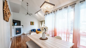 Ein modernes Wohnzimmer mit Kamin, Esstisch mit Stühlen, einer Couch und einem Deckenventilator.