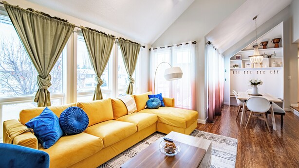 Ein helles Wohnzimmer mit einem gelben Sofa, blauen Kissen und einem Holztisch.