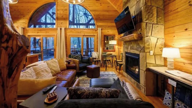 Un acogedor interior de cabaña de madera con chimenea, asientos cómodos y ventanas amplias.