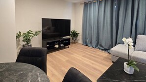 A modern living room with a flat-screen TV, a grey sofa, a round marble table, and two potted plants. - Room-single Guest Room in Upper Hutt (Upper Hutt)