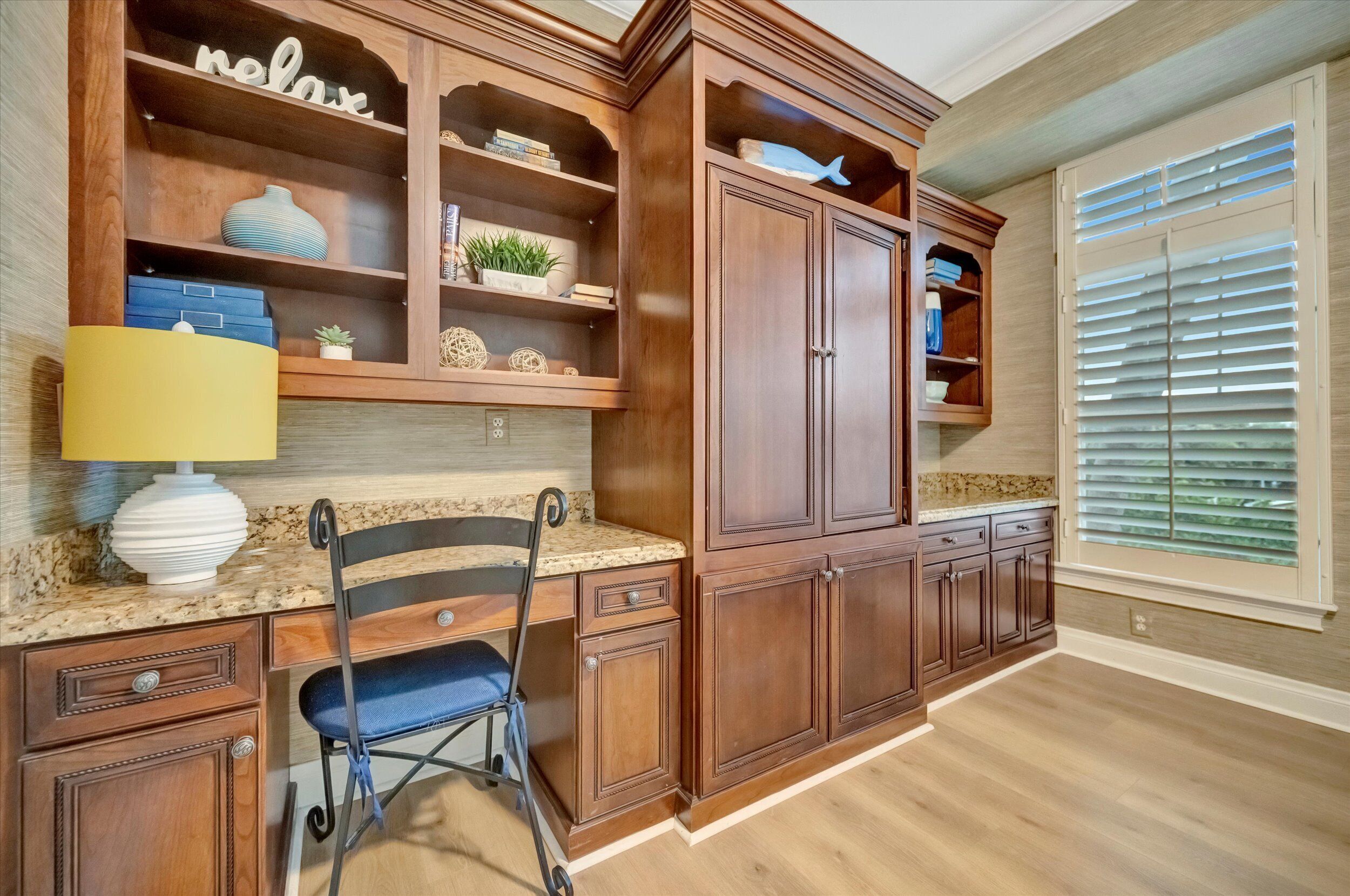 Una cocina con armarios de madera, encimera de granito, una silla y una ventana con persianas.