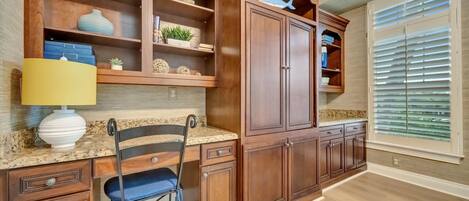 Una cocina con armarios de madera, encimera de granito, una silla y una ventana con persianas.