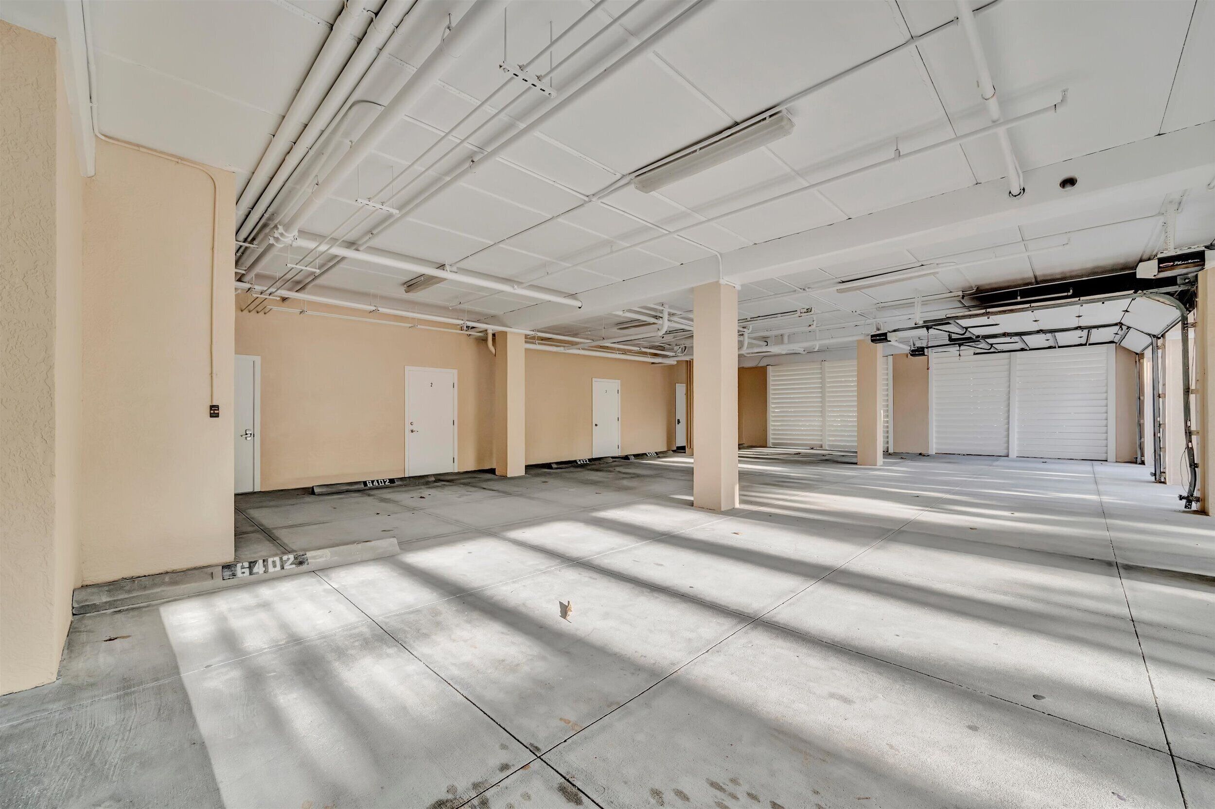A spacious indoor area with concrete floors, beige walls, and white ceilings with exposed pipes.