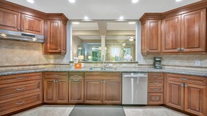 A modern kitchen with wooden cabinets, granite countertops, and a stainless steel dishwasher. - Holmes Beachfront Oasis (Holmes Beach)