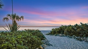 A pathway leading to a beach with a sunset view, surrounded by greenery and rocks. - Holmes Beachfront Oasis (Holmes Beach)