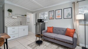 Et moderne køkken med hvide skabe, en grå sofa med orange puder og et lille rundt bord.