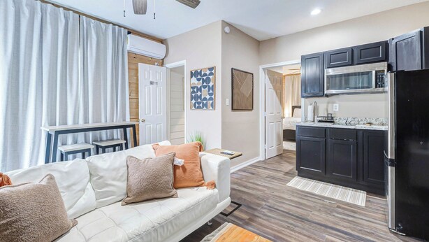 A modern living room with a white sofa, a coffee table, and a kitchen area with dark cabinets and a black refrigerator. - Houston Private Retreat, 17 min Downtown (Houston)