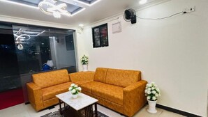 A living room with a sectional sofa, a coffee table, and two potted plants. - HOTEL IHAM PARADISE (Mangaluru)