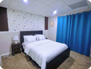 Ein Schlafzimmer mit einem Bett, einem Nachttisch, einer Lampe, einer Wand mit geometrischen Mustern und blauen Vorhängen.
