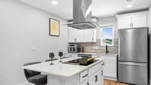 A modern kitchen with white cabinetry, a stainless steel refrigerator, and a central island with a microwave and toaster. - Cozy 1-bedroom apartment in beautiful Gulf Breeze with AC (Gulf Breeze)