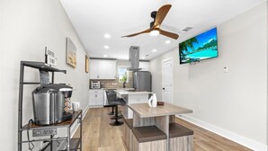 A modern kitchen with a coffee station, a dining area with a wooden table, and a ceiling fan. - Cozy 1-bedroom apartment in beautiful Gulf Breeze with AC (Gulf Breeze)