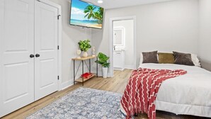 A bedroom with a bed, a TV mounted on the wall, a ceiling fan, and a door. - Cozy 1-bedroom apartment in beautiful Gulf Breeze with AC (Gulf Breeze)