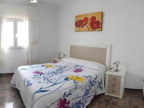 A bedroom with a bed, a nightstand, a bedside table, a window with curtains, and a painting on the wall. - Sea-view Apartment With Terrace (Conil de la Frontera)