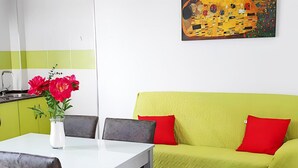 A dining area with a white table, two chairs, a vase with red flowers, and a green sofa with red cushions. - Sea-view Apartment With Terrace (Conil de la Frontera)