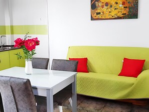 A dining area with a white table, two chairs, a vase with red flowers, and a green sofa with red cushions. - Sea-view Apartment With Terrace (Conil de la Frontera)