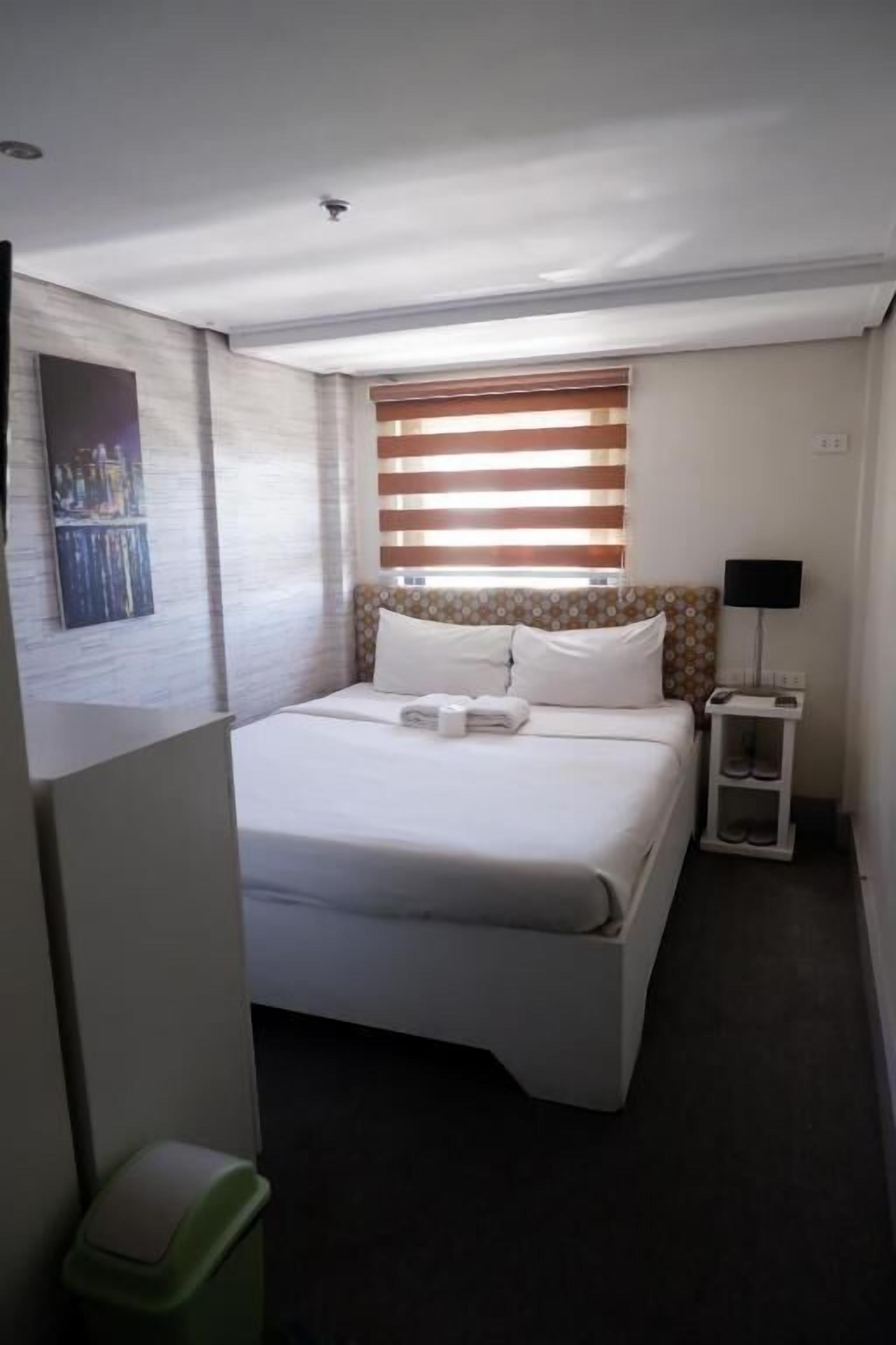 A neatly arranged hotel room with a bed, a bedside table with a lamp, and a wall-mounted painting.