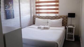 A neatly arranged hotel room with a bed, a bedside table with a lamp, and a wall-mounted painting.