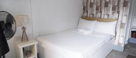 Un letto singolo con biancheria bianca, un comodino con una lampada e un condizionatore d'aria a parete.