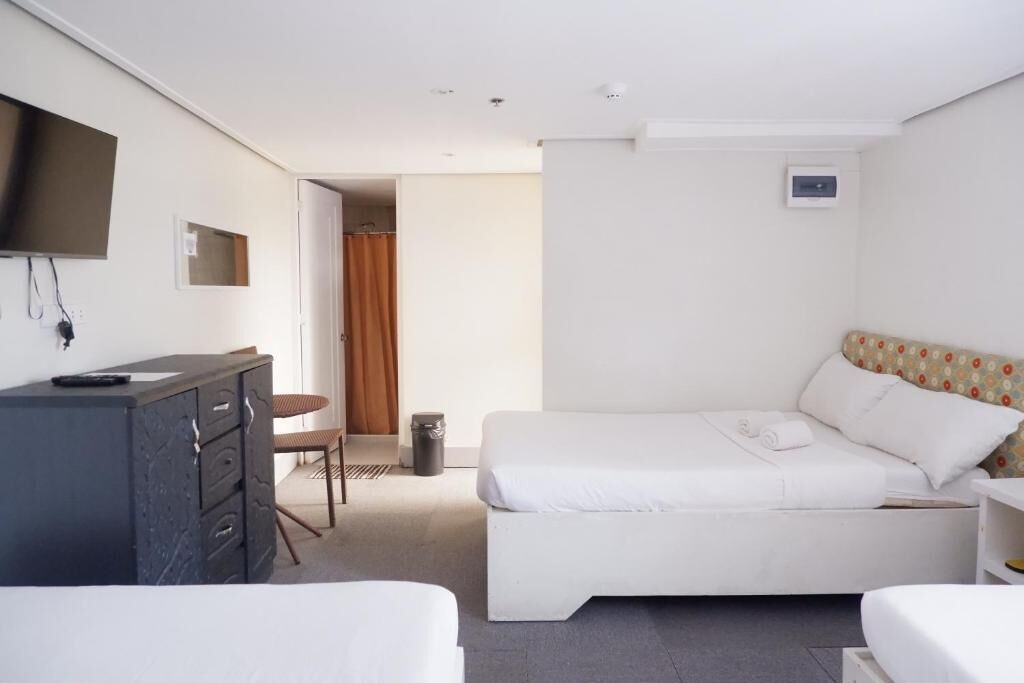 A hotel room with a bed, a desk, a chair, a TV mounted on the wall, and a small window.