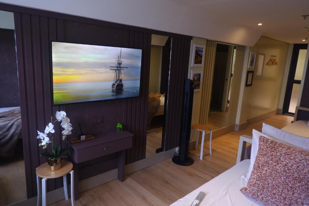 A modern hotel room with a large mirror, a painting of a ship on the wall, a small table with a vase of flowers, and a bed with a patterned pillow.