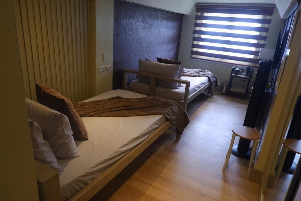 A bedroom with a bed, a sofa, a small table, and a window with blinds.