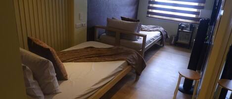 A bedroom with a bed, a sofa, a small table, and a window with blinds.