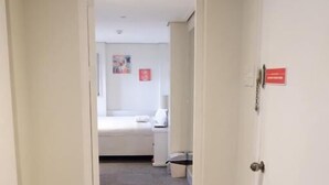A hallway leading to a bedroom with a bed, a nightstand, and a small table.