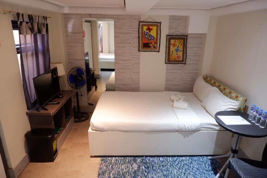 A hotel room with a bed, a desk, a TV, and a fan.