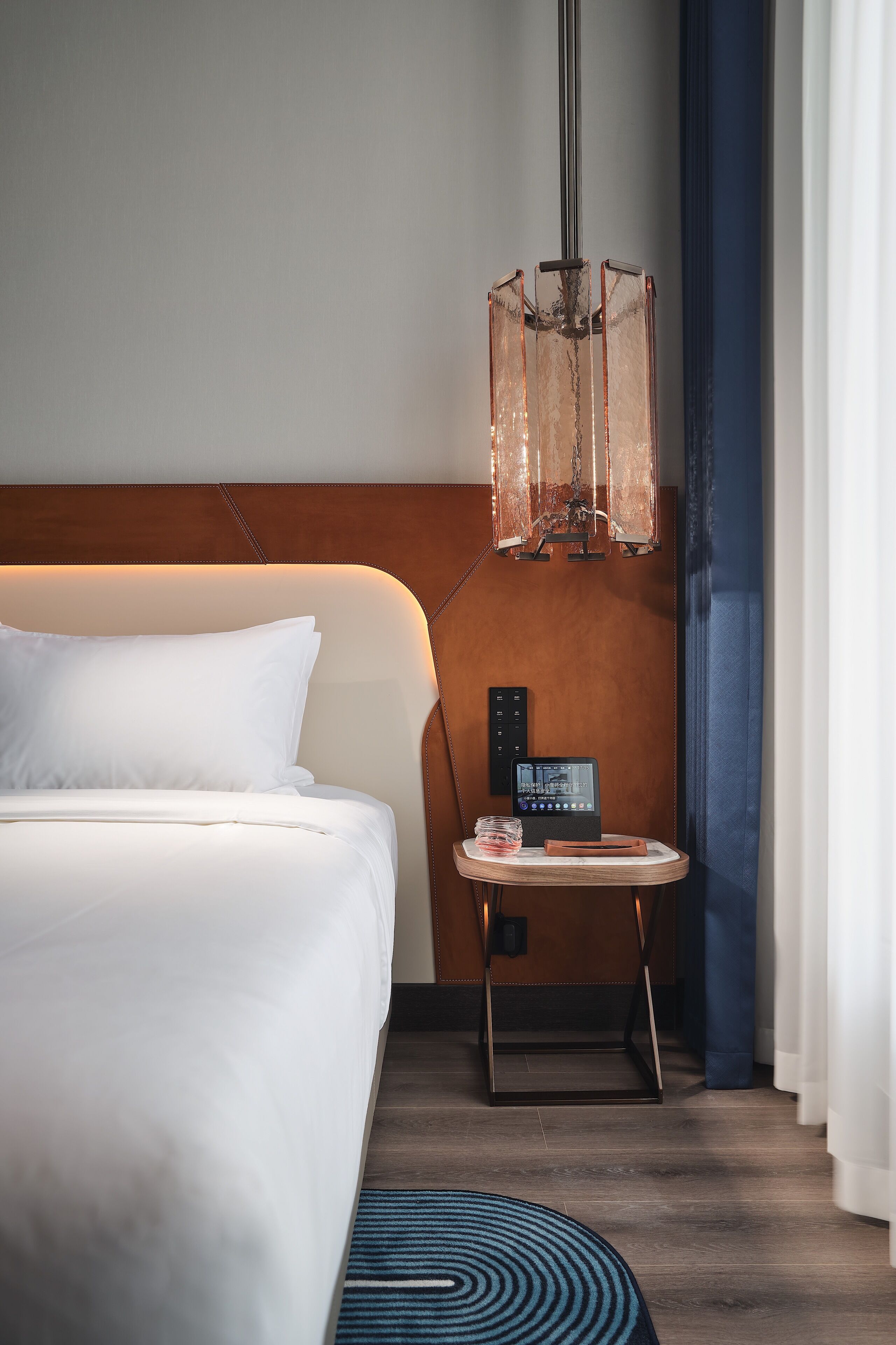 A hotel room with a bed, a bedside table with a lamp, and a control panel.