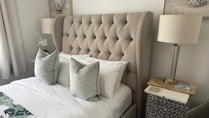 Un lit bien fait, avec une tête de lit capitonnée, une table de chevet avec une lampe et une commode décorée.