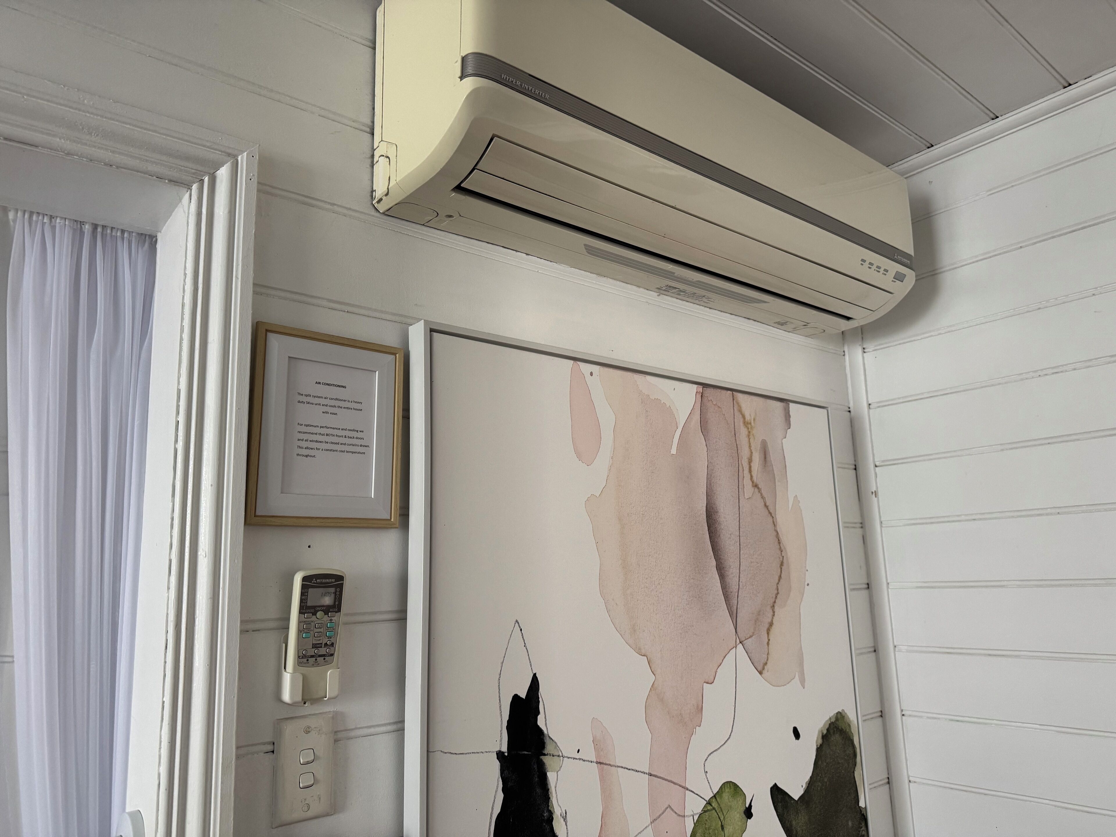 A room with a ceiling-mounted air conditioner, a framed informational poster, a thermostat, and a wall-mounted phone.
