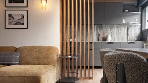 A modern living room with a sofa, a coffee table, and a patterned rug. There is a kitchen area with a countertop and cabinets visible through a wooden partition. - Santos Megève near the village (Megève)