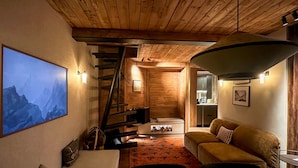 A cozy interior with a wooden staircase, a sofa, a coffee table, and a large wall-mounted TV. - Santos Megève near the village (Megève)