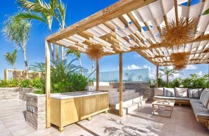An outdoor patio with a wooden pergola, a built-in bar, and a seating area with a sofa and coffee table. - Stylish Apt w/ In-Unit Laundry • Rooftop Pool (Playa del Carmen,)