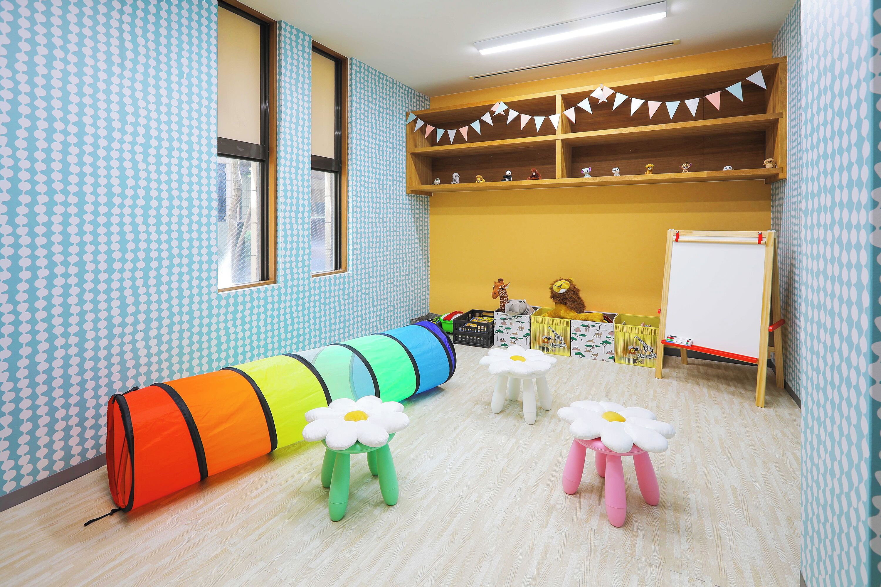A room with patterned wallpaper, a window, a whiteboard, and a shelf with toys.