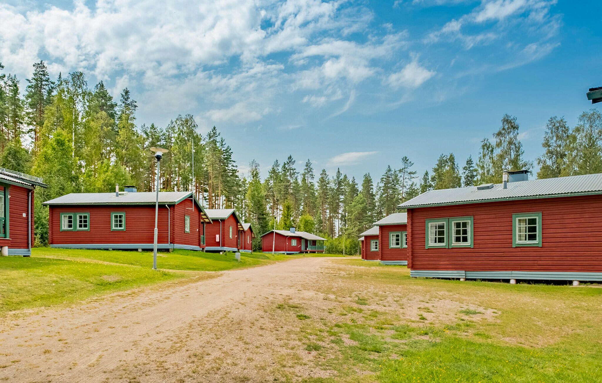 En rad röda stugor med grön dekor, omgivna av en grusväg och en tät skog.