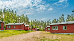 A row of red cabins with green trim, surrounded by a dirt path and dense forest. - Amazing home in Ekshärad with WiFi (Ekshärad)