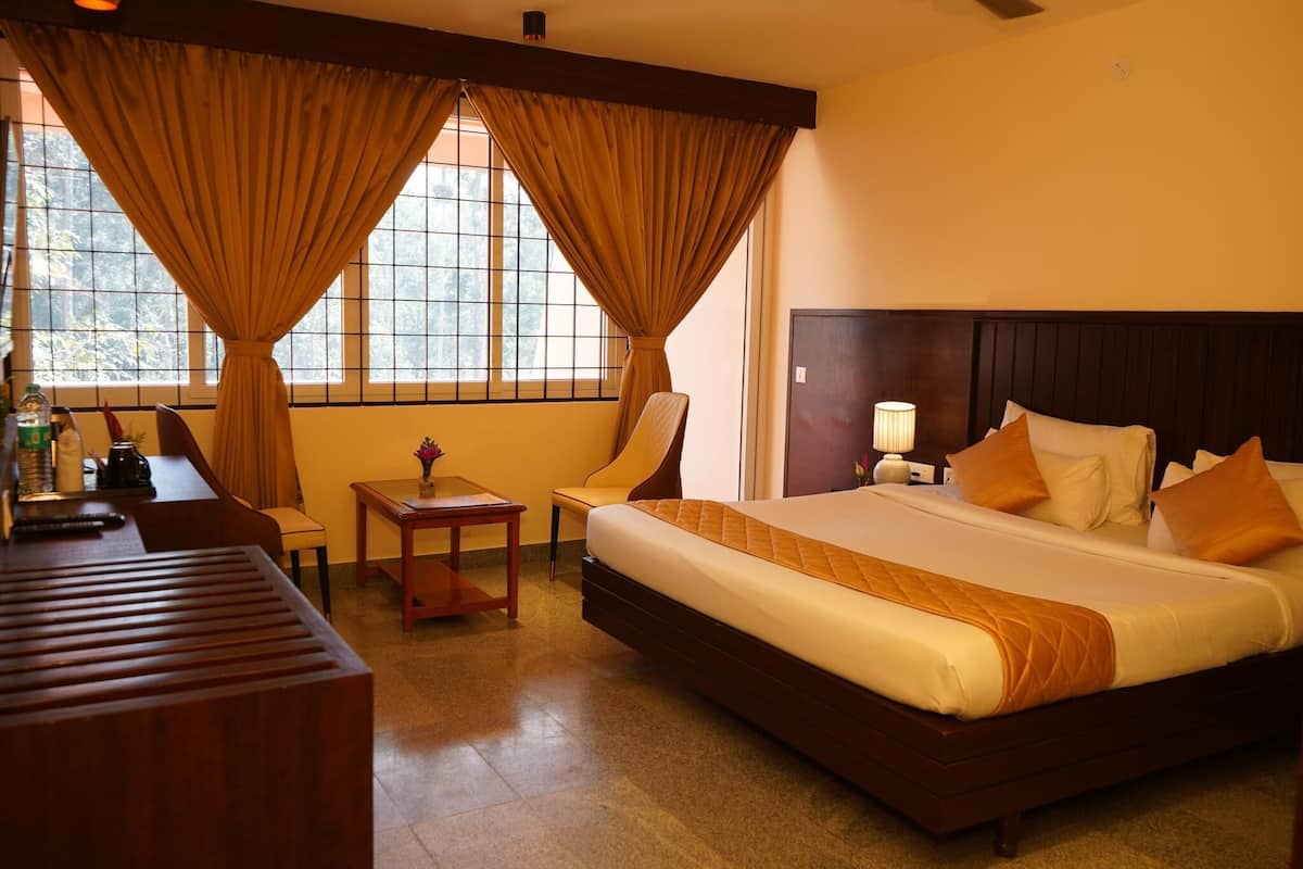 A hotel room with a large bed, a desk, a chair, a lamp, and a window with curtains.
