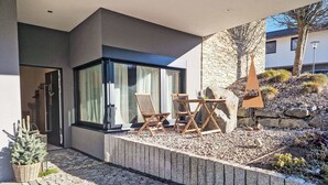 Ein moderner Außenbereich mit einer Steinwand, einem Holztisch und zwei Holzstühlen.