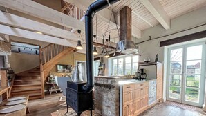 Une cuisine spacieuse dotée d’un poêle à bois central, d’un mur en pierre décoratif et d’une grande fenêtre qui laisse entrer la lumière naturelle.