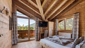 Een houten slaapkamer met een bed, een televisie en een balkon met uitzicht op de bergen.