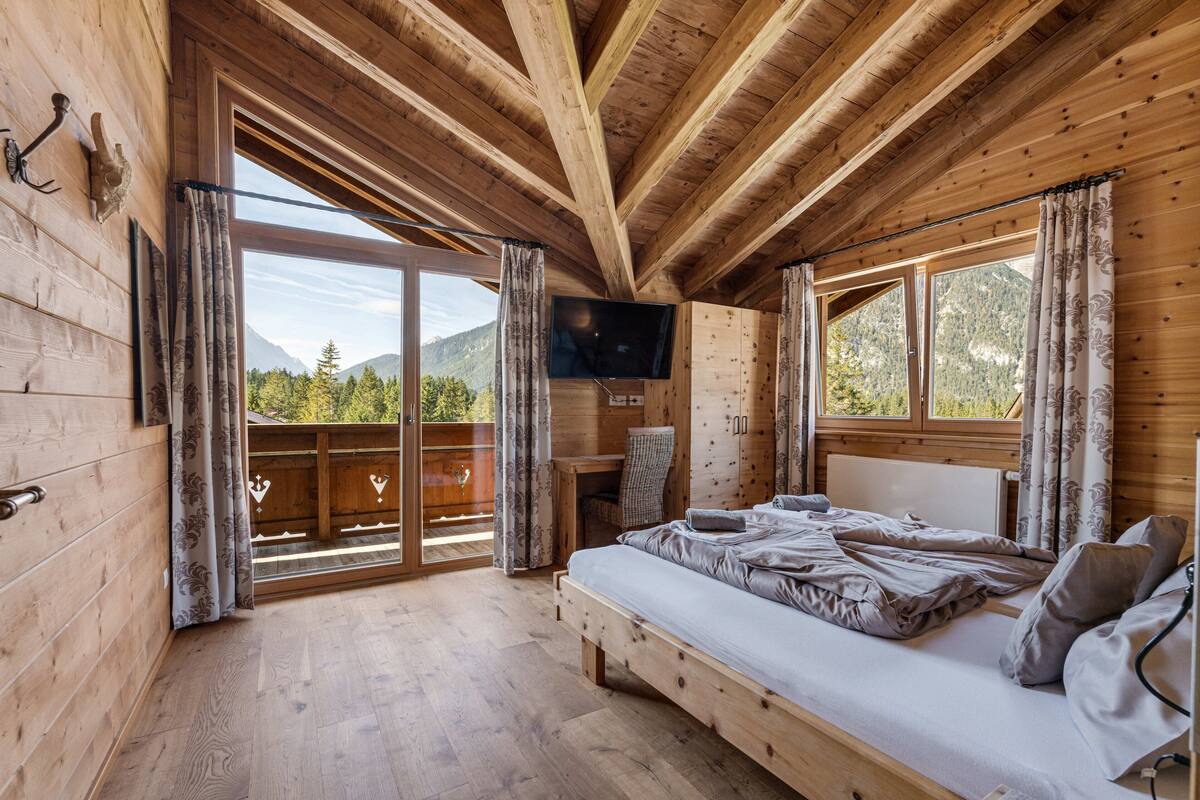 Een houten slaapkamer met een bed, een televisie en een balkon met uitzicht op de bergen.