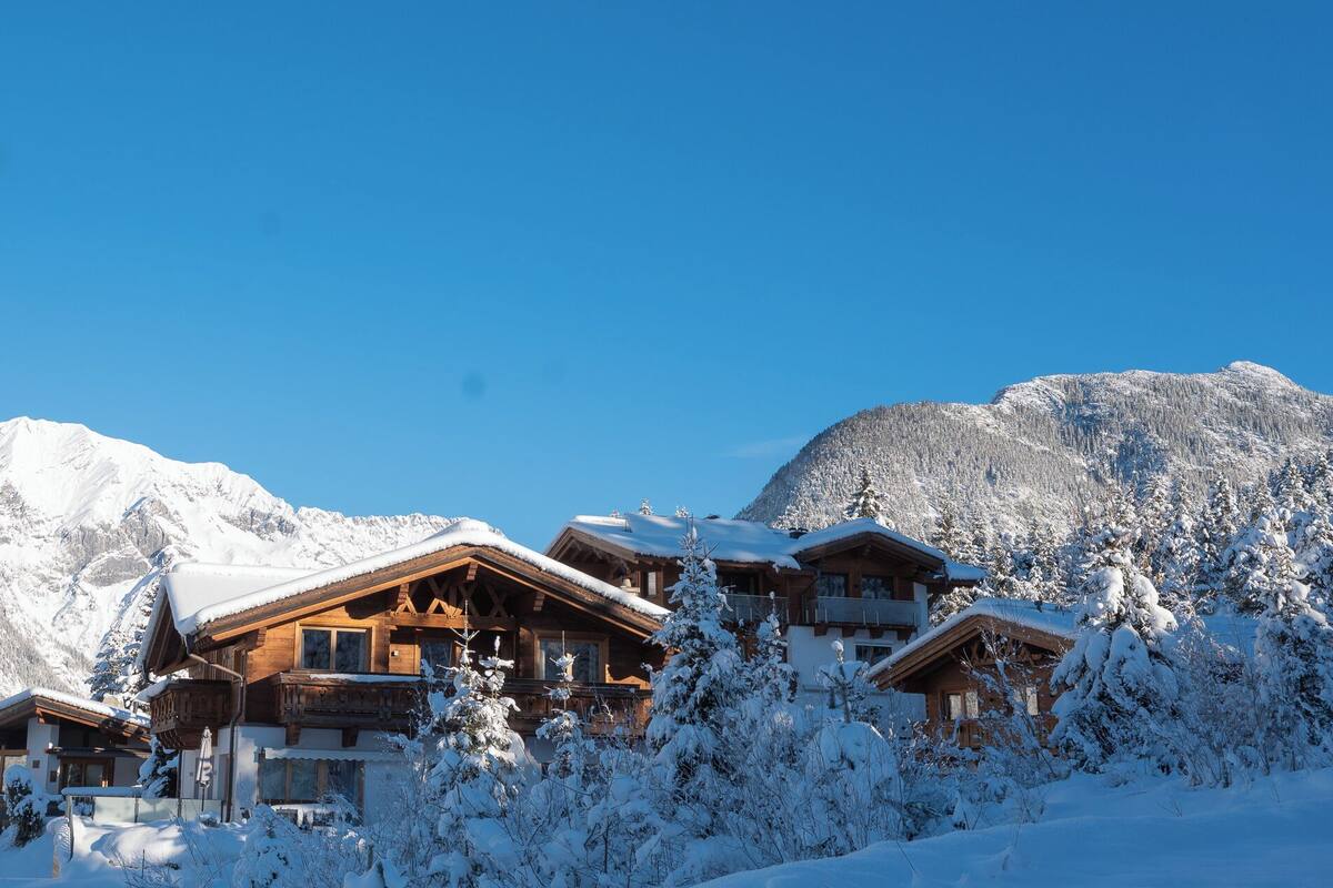 Een houten chalet met meerdere balkons, omgeven door sneeuwbedekte bomen en bergen op de achtergrond.