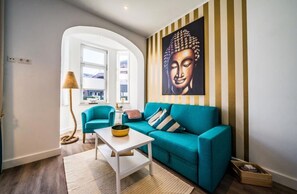 A modern living room with a teal sofa, a white coffee table, and a large Buddha painting on the wall. - Vacation apartment "Ocean" in the heart of Borkum, vacation with dog - Ria's BeachVilla (Borkum)