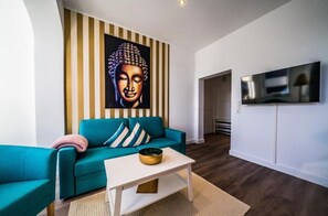 Un salón con un sofá color turquesa, una mesa de centro blanca y una pintura de Buda en la pared.