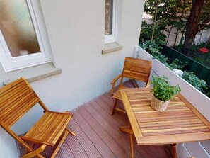 Eine Holzterrasse mit zwei Stühlen, einem Tisch, einem Blumentopf und Blick auf einen Garten und Bäume.